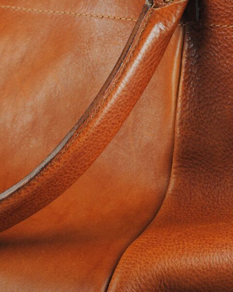 Detail close-up of a warm tan leather bag showing the handle stitching and smooth natural grain
