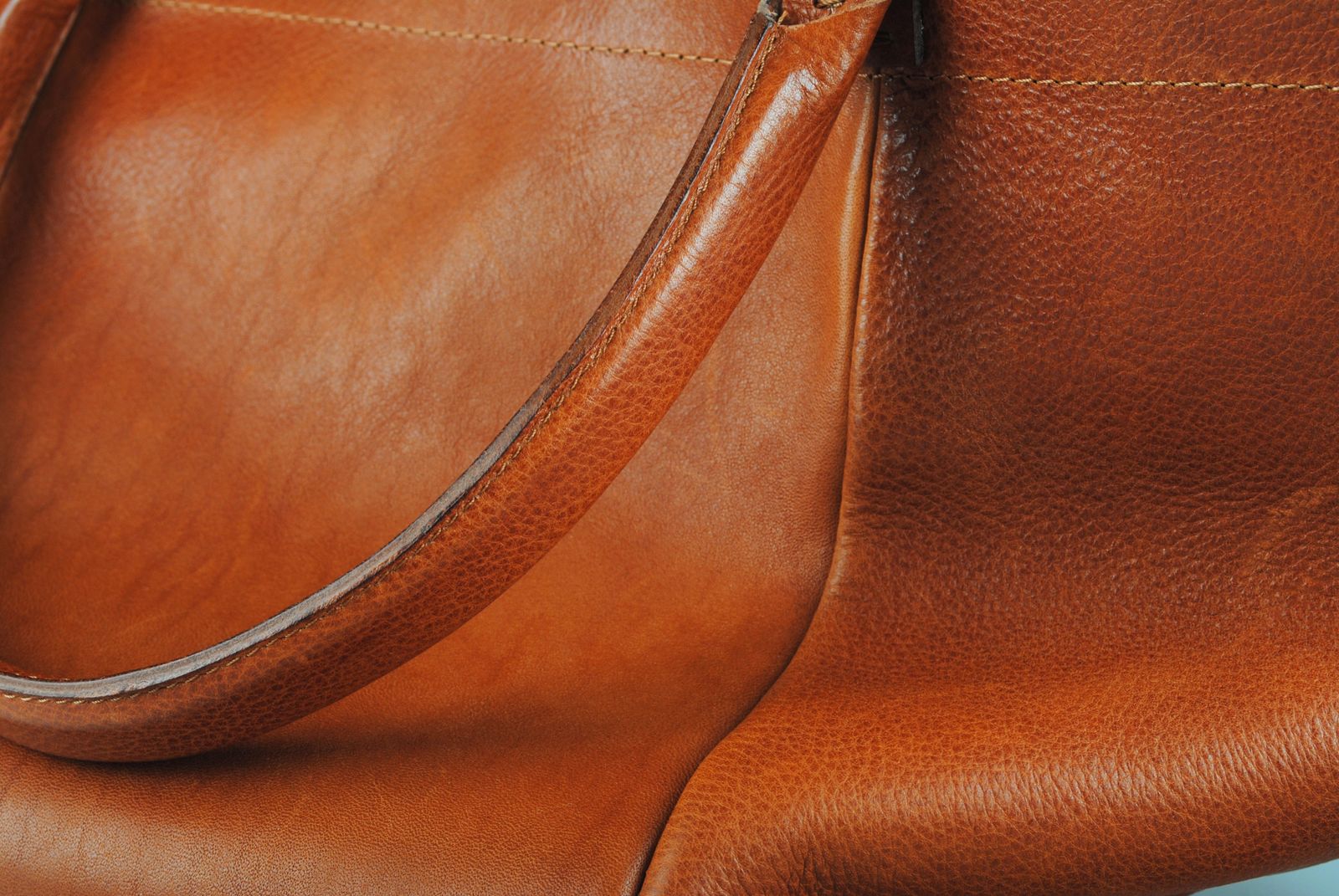Detail close-up of a warm tan leather bag showing the handle stitching and smooth natural grain