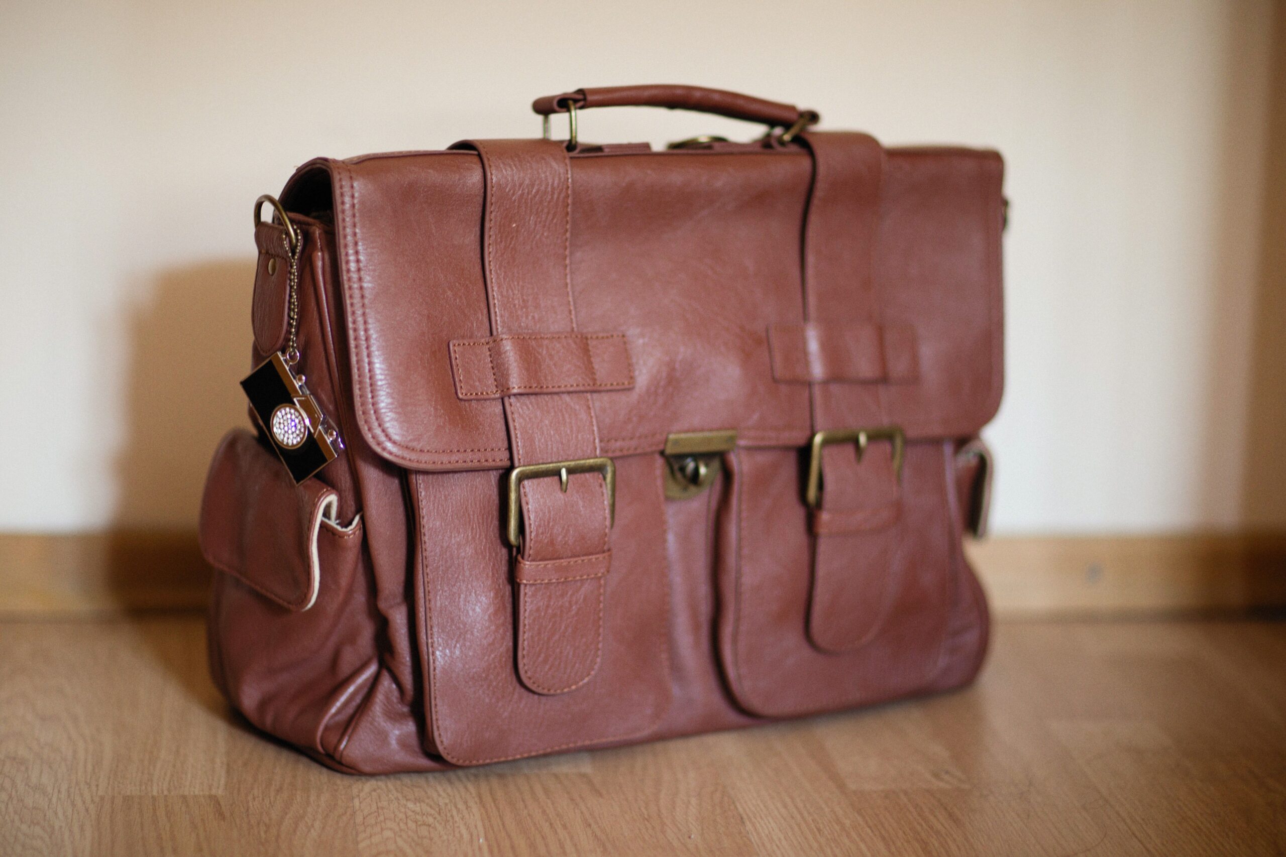Traditional English-style brown leather satchel with brass buckles on a wooden floor