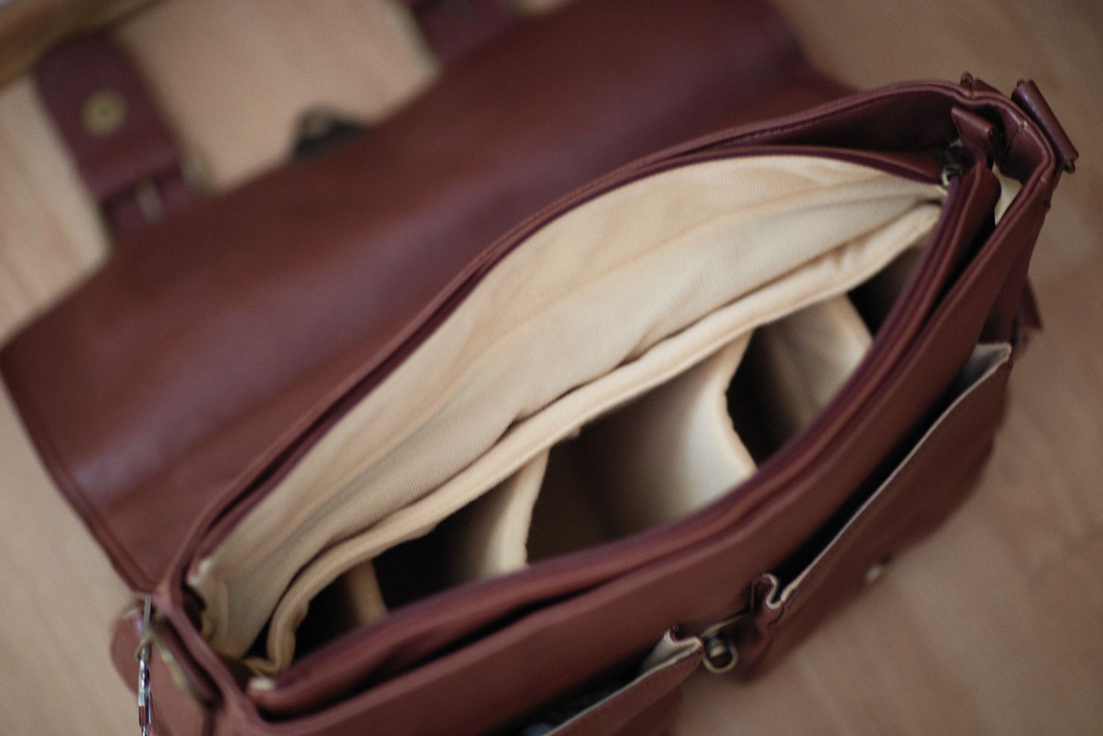 Overhead view into an open brown leather satchel-style briefcase, showing the cream lining and organised interior pockets