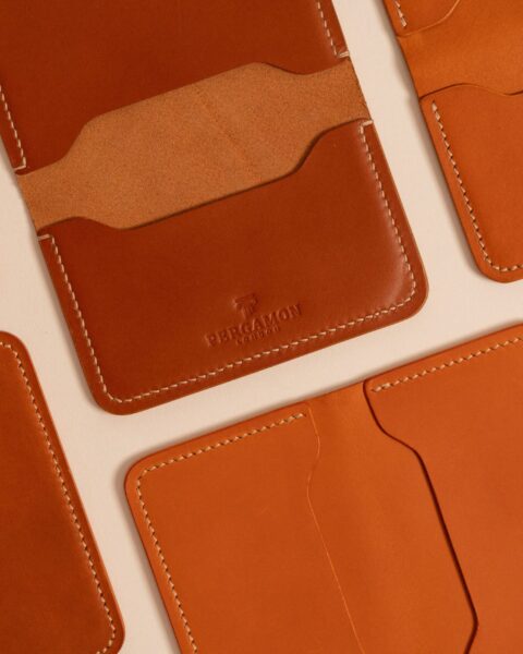 Close-up of stitched tan leather cardholders and wallets on a light background