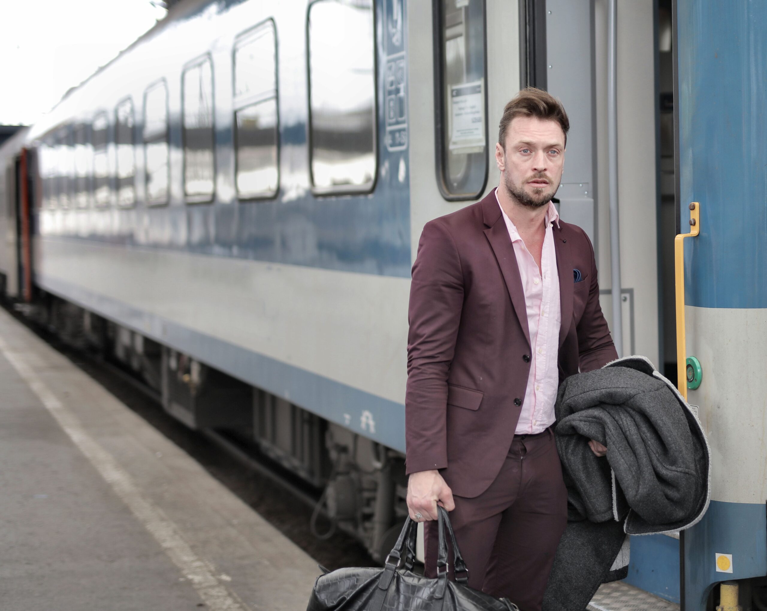 Man in a suit exiting a train platform, carrying a black leather holdall bag