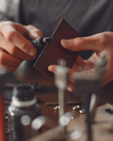Close-up of an artisan's hands hand-painting and polishing a leather edge at a workbench