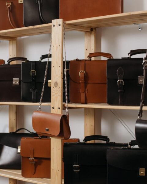 A row of brown and black leather briefcases displayed on wooden shelves in a workshop