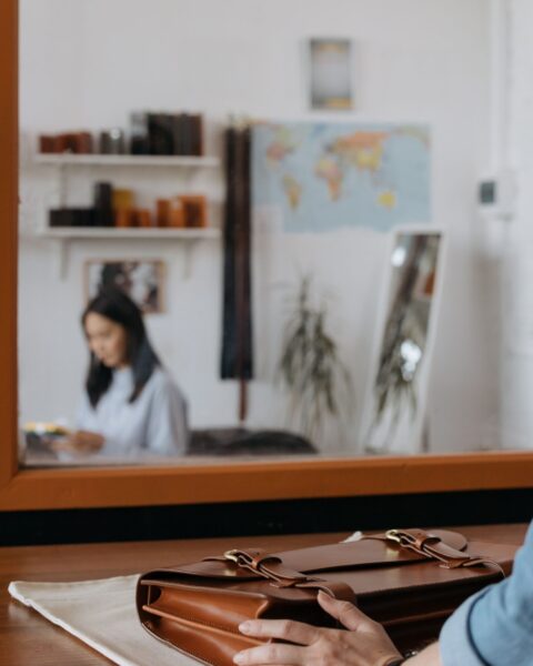 Brown leather briefcase on a wooden desk with a leather workshop visible in the background