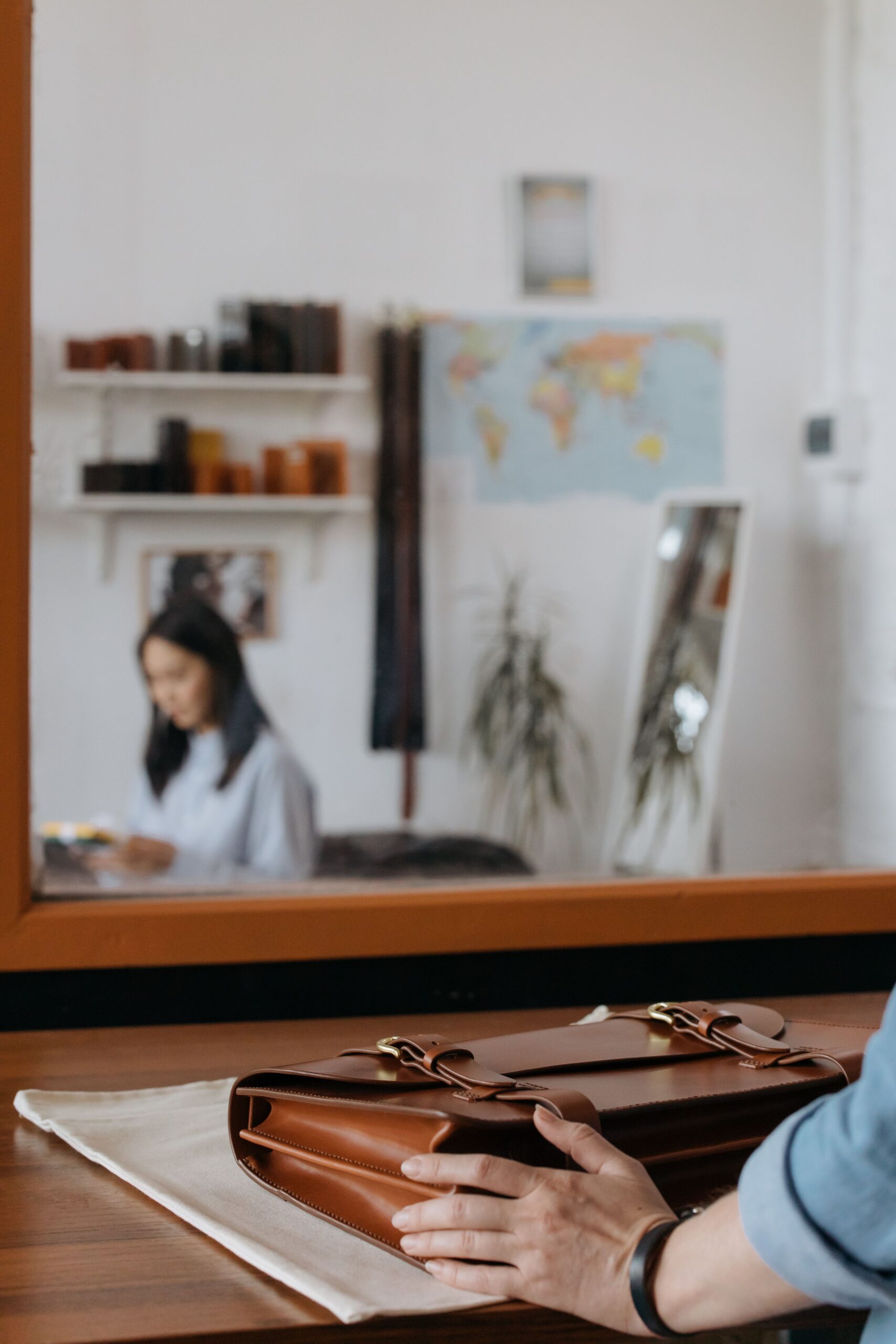 Brown leather briefcase on a wooden desk with a leather workshop visible in the background