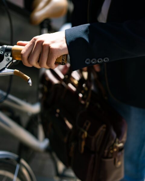 Close-up of a man in a suit holding a bicycle handlebar and a brown leather briefcase
