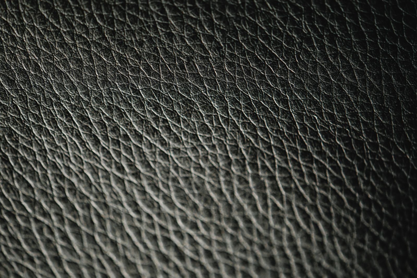Close-up macro shot of black leather showing a cross-hatch, diamond-textured pattern pressed into the surface