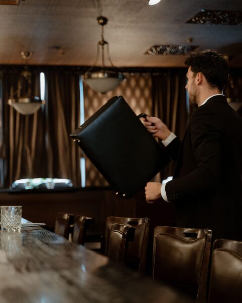 Man in a suit carrying a black leather briefcase in a dimly lit upscale restaurant