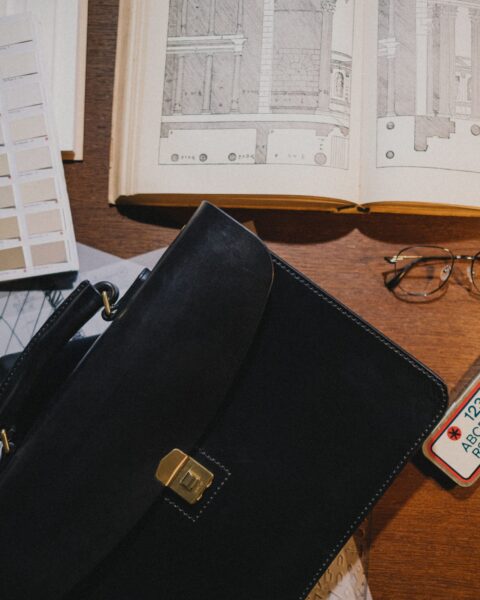 Black leather briefcase on a desk with an architecture book and glasses, minimalist design styling