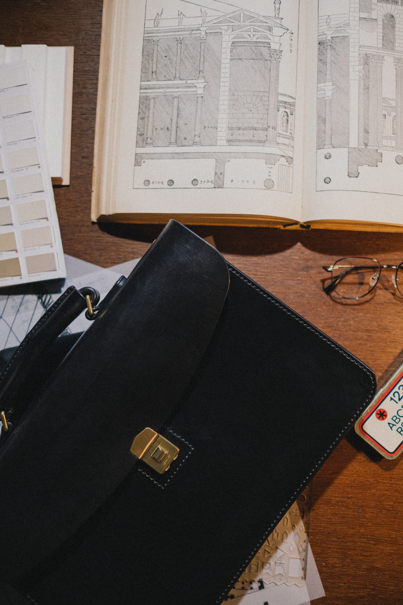 Black leather briefcase on a desk with an architecture book and glasses, minimalist design styling