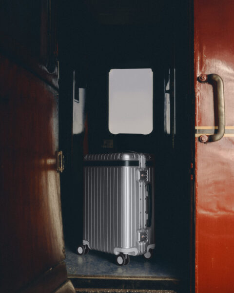 Three Carl Friedrik aluminium Carry-on cases stacked on a train seat by a window