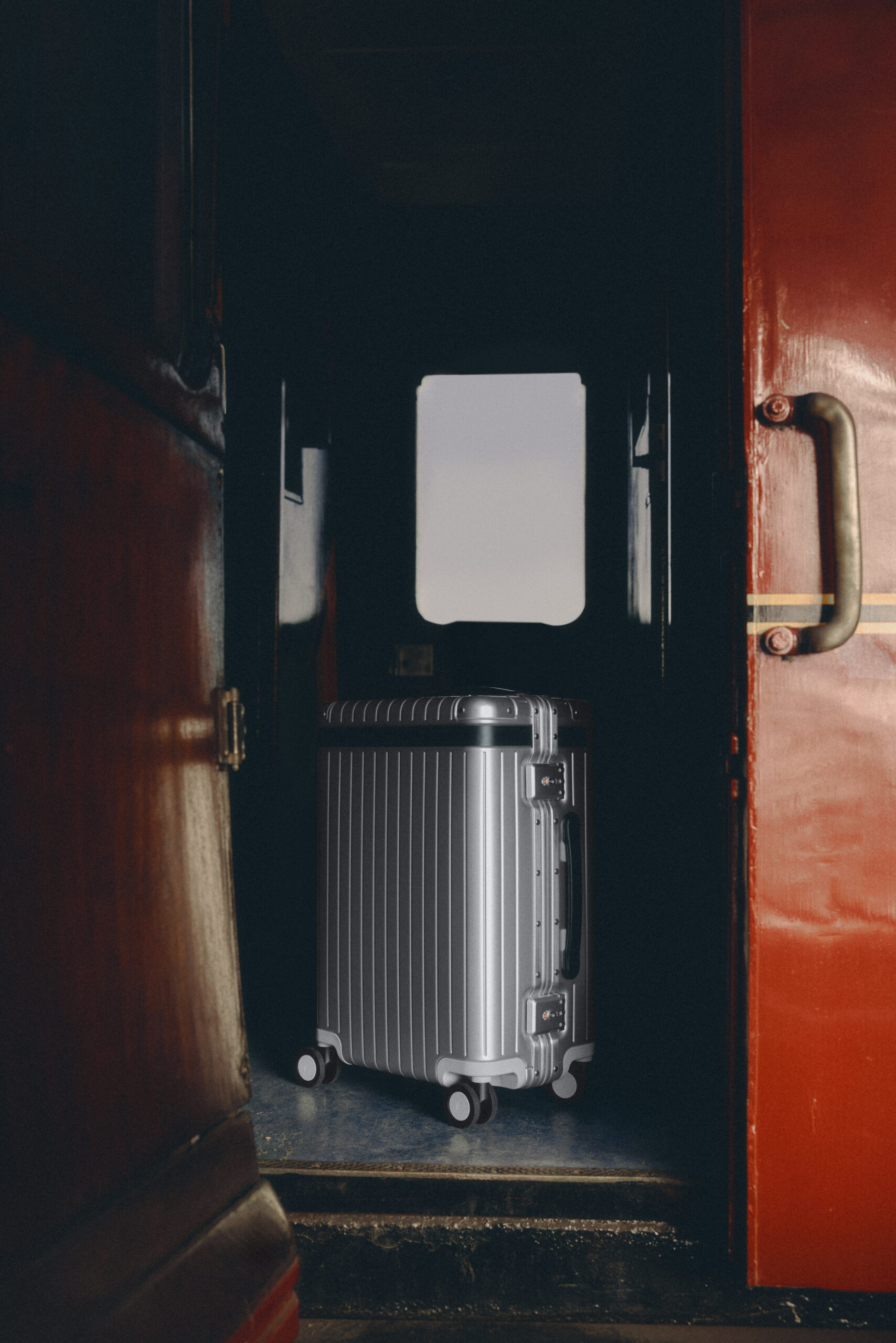 Three Carl Friedrik aluminium Carry-on cases stacked on a train seat by a window