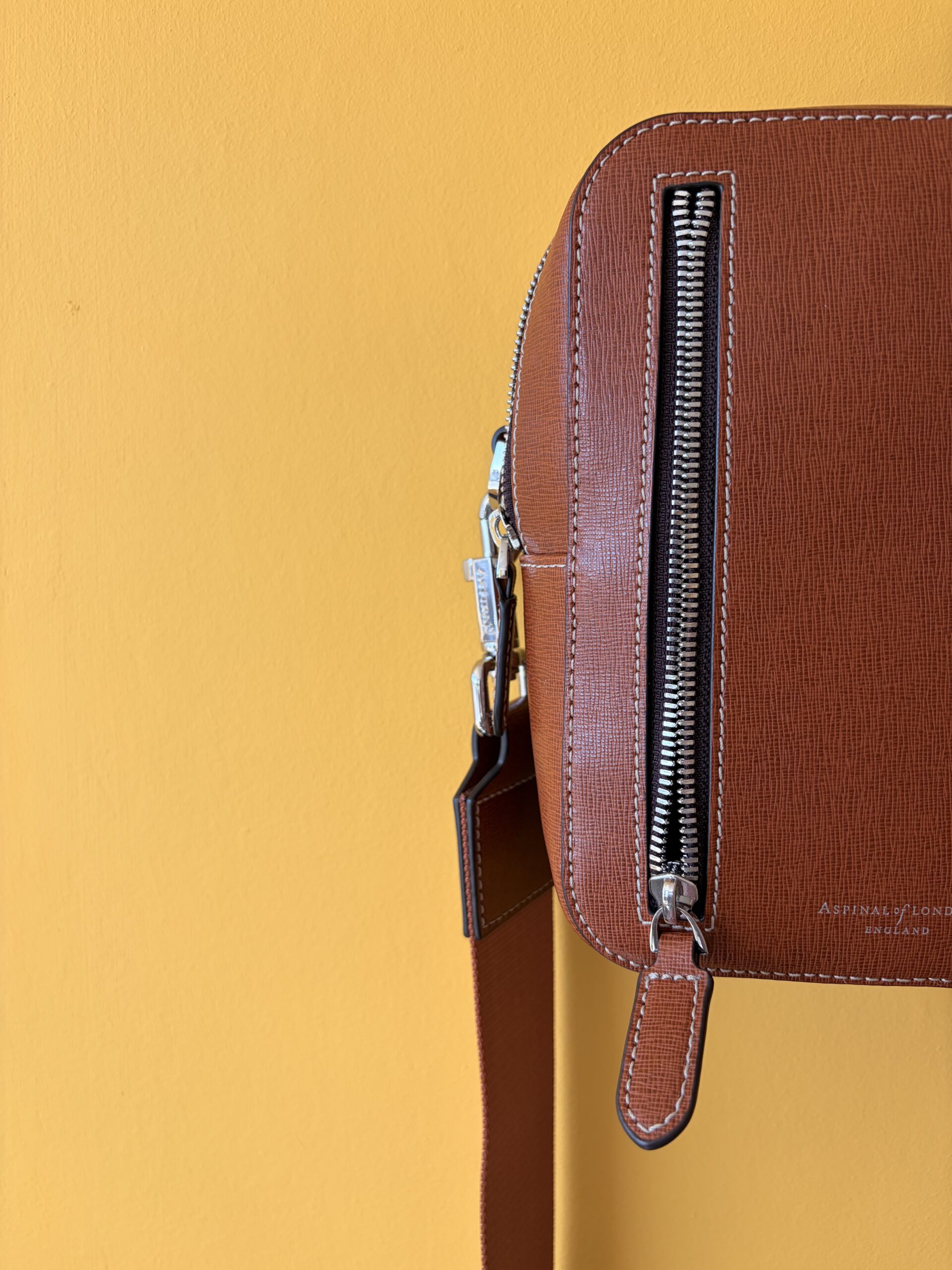 The Aspinal Reporter North South's front zip pocket, strap and silver-toned hardware