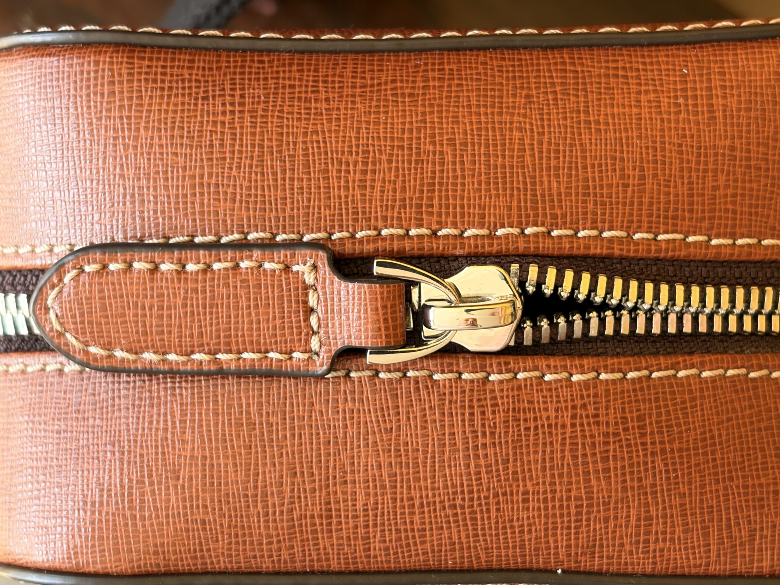 Top-down close-up of the front pocket zip fully open, showing the pocket mouth still barely parted against the tan saffiano cross-hatch texture