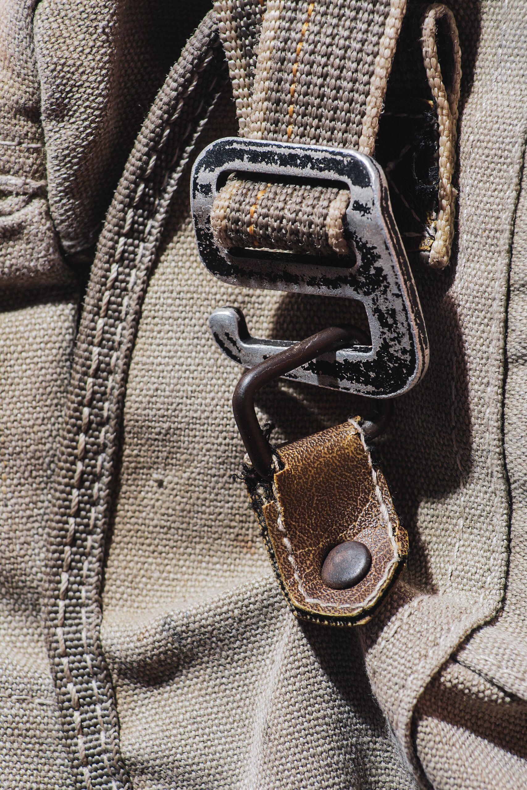 Close-up of a metal hook buckle and military-style webbing strap on a rugged canvas bag