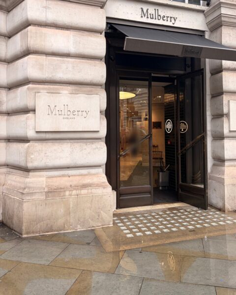 Mulberry's Regent Street shopfront on a wet day, with "Mulberry England" carved into the stone and the doors open under a black awning