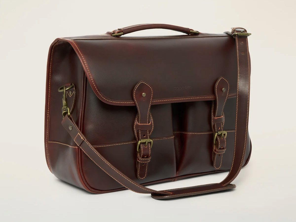 Tusting Leather Clipper (Large) in Sundance Floodlight leather, three-quarter view showing the flap, two buckled straps over twin front pockets and the shoulder strap