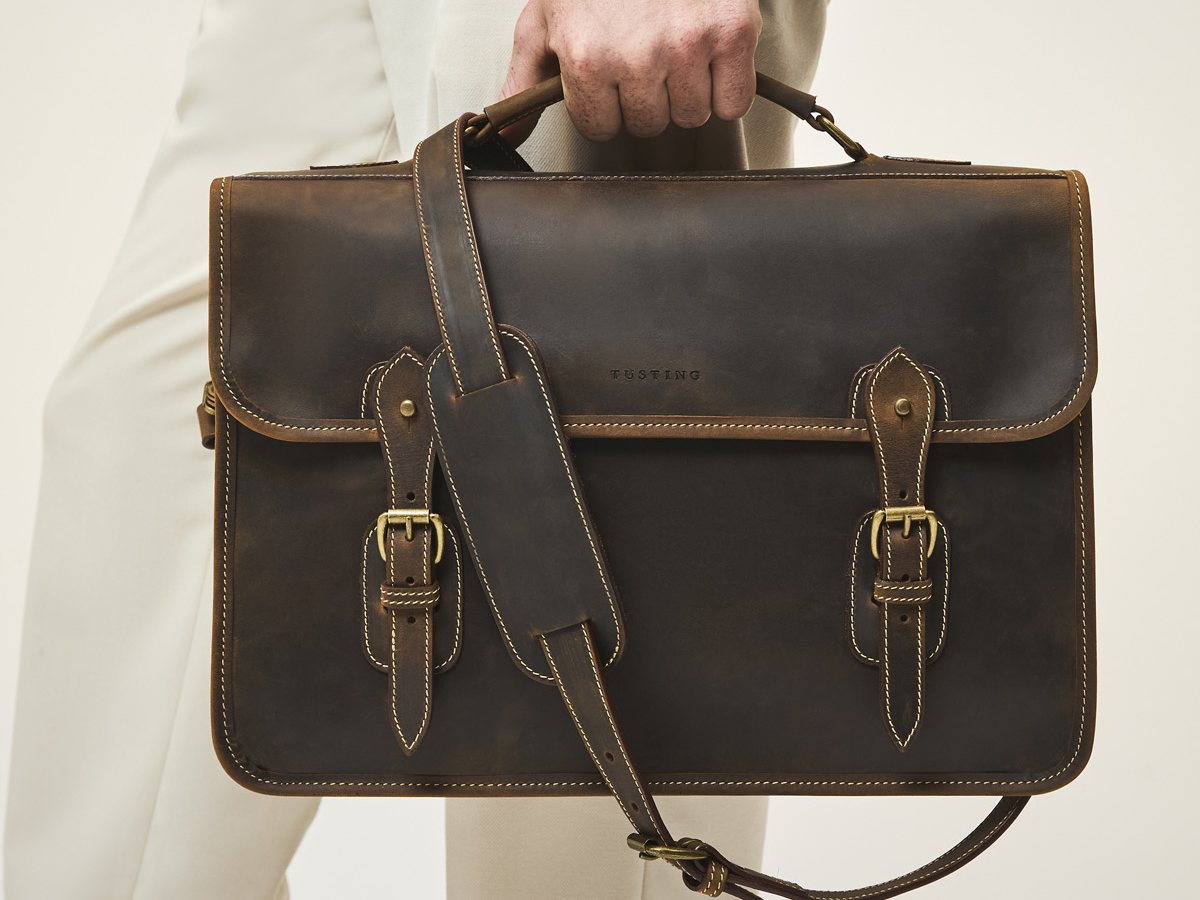 Tusting Wymington briefcase in Aztec Crazyhorse leather carried by its top handle, with the shoulder strap hanging across the front
